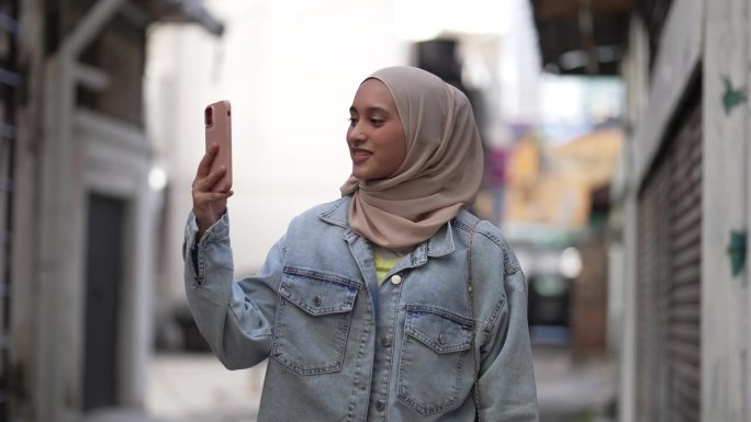 戴着头巾的亚洲马来妇女用智能手机在街上拍照