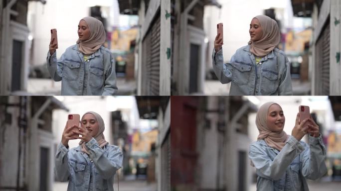 戴着头巾的亚洲马来妇女用智能手机在街上拍照