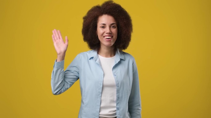 年轻的微笑的非裔美国妇女握手说再见站在橙色的工作室背景