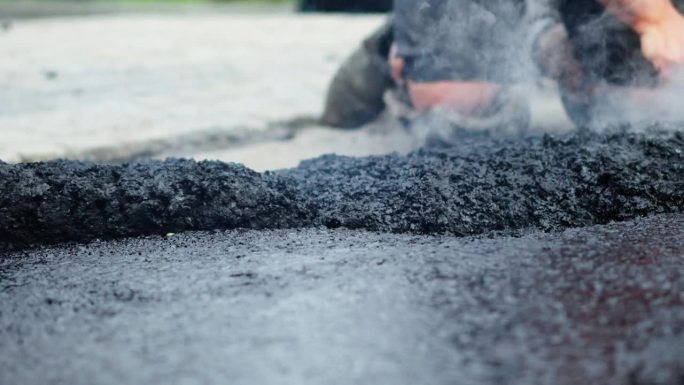 道路施工工人在铺路工处手动在地面上铺装和调整热沥青或沥青