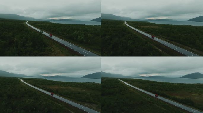红色越野车独自驾驶，行驶在空旷的道路与史诗般的北欧景观在灰色的天。无人机航拍图。