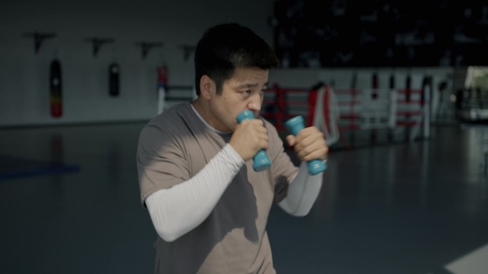 年轻的亚洲男子在健身房拿着哑铃练习拳击动作