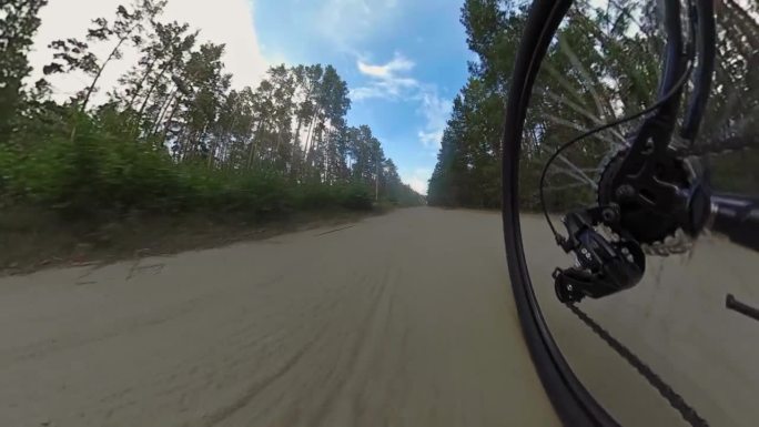 骑自行车的人骑越野山地车沿着未铺设的土沙路在森林。链传动，带卡带的后变速器。换挡杆。骑师轮子。Cog