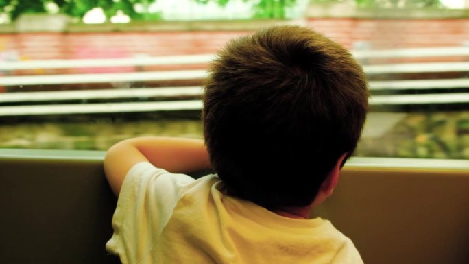 一个五岁的男孩乘坐地面地铁，开车进入隧道，向窗外望去。