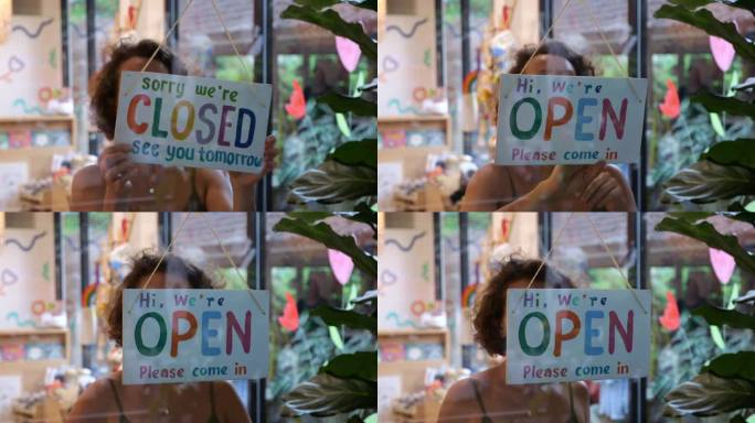 一名白人妇女将一家商店前门上的彩色方形标志从关门变为开门。早上，卖家打开商店的门，拧了拧玻璃上邀请买
