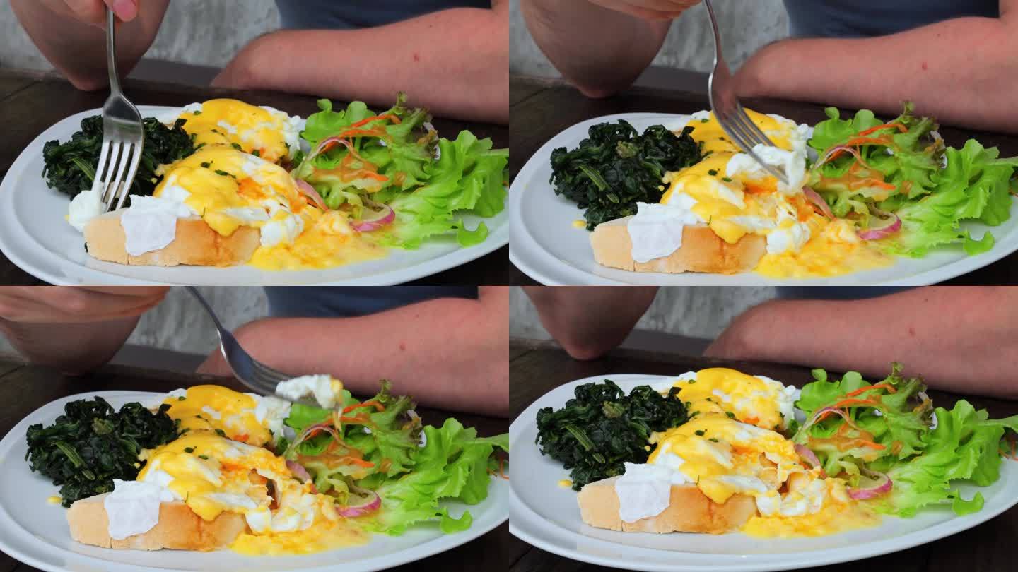 特写镜头男子用叉子扎起一块荷包蛋，蘸上蛋黄。男士早餐在餐厅吃荷包蛋，沙拉配番茄黄瓜洋葱吃荷包蛋可以保