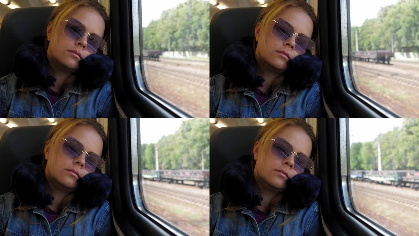 一位戴着太阳镜、抱着旅行颈枕的疲惫的年轻女子在火车上睡觉。