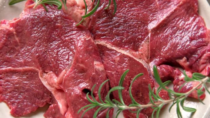 红肉俯视图。切好的牛排在木制砧板上旋转。平的。新鲜的生肉加上香料和香草。黑安格斯牛排上等肉t骨，纽约