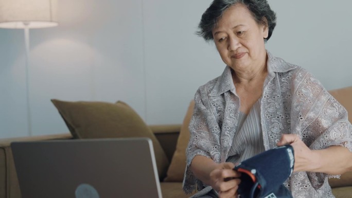 欢快的奶奶在客厅用电脑和医生交谈的正面画面。她自己测量血压和心率，并询问药物。