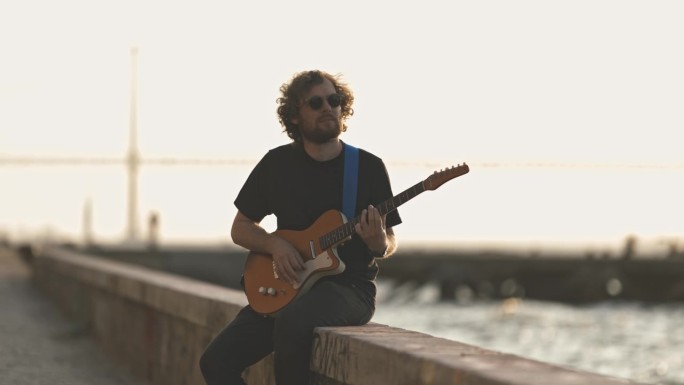一个人坐在海边，在日落时分弹吉他