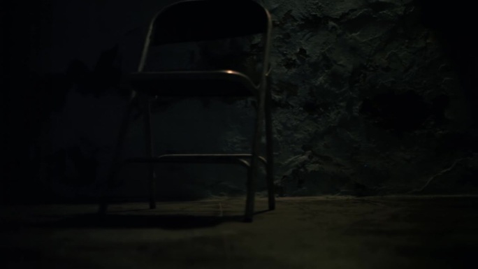 金属椅子在表面上自我移动的剪影。不寻常的恐怖电影般的椅子移动或拉动镜头。黑暗的阁楼房间与一个单一的光