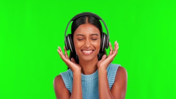 快乐的女人，戴着耳机，伴着绿屏上的音乐跳舞，背景是摄影棚。女性微笑的肖像与耳机听音频流，歌曲或声音轨