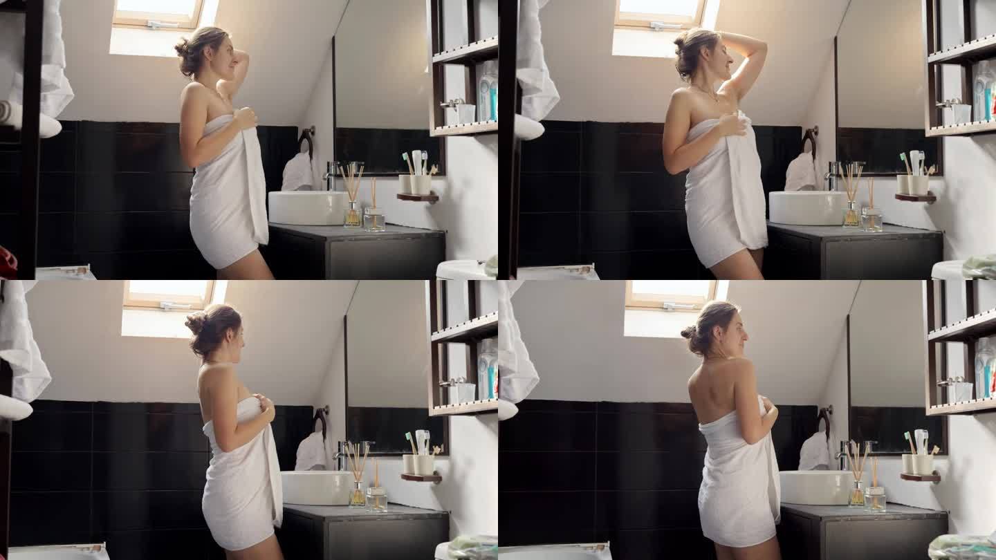 一个裹着毛巾的女人，站在浴缸里，对着镜子审视自己。女性卫生和自我保健程序