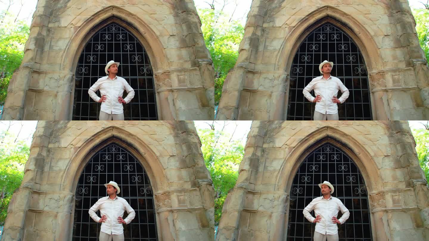 一个戴着白色草帽的男人站在一座古老的哥特式建筑前，若有所思地转过头来。追求。地下室