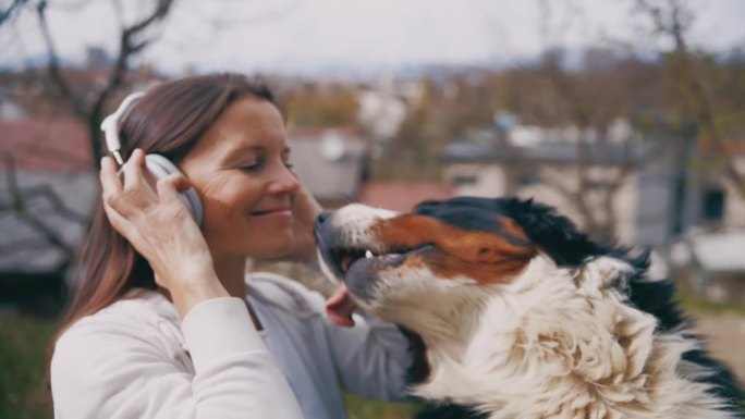 在阳光明媚的城市公园里，快乐的女人带着耳机和狗