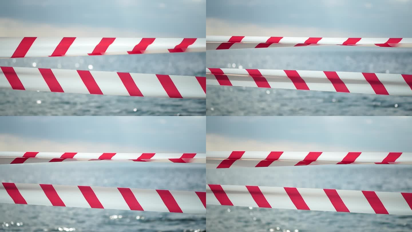 红白警示带屏障带随风飘动，飘过异域风情的海边，背景中没有人。红白警戒线禁止进入。没有度假的想法，推迟