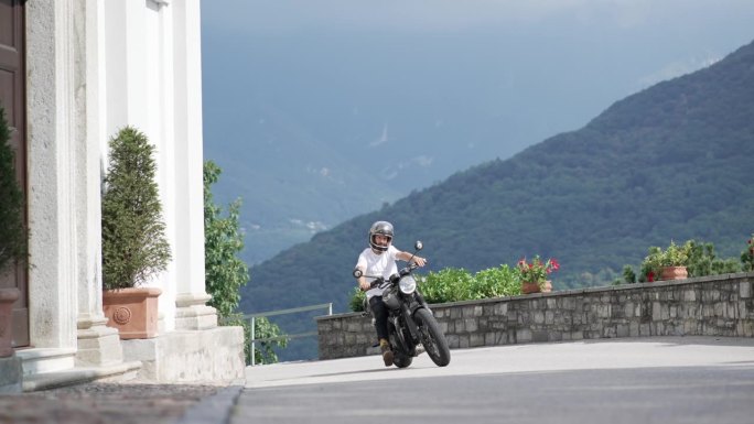 变焦镜头中，一名男子骑着摩托车，在平坦的道路上穿过古老的村庄