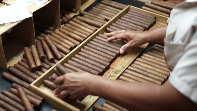 近距离慢镜头，黑人女性的手把刚卷好大小的雪茄放在木托盘里，等待贴上标签和装盒。优质手工古巴雪茄工厂