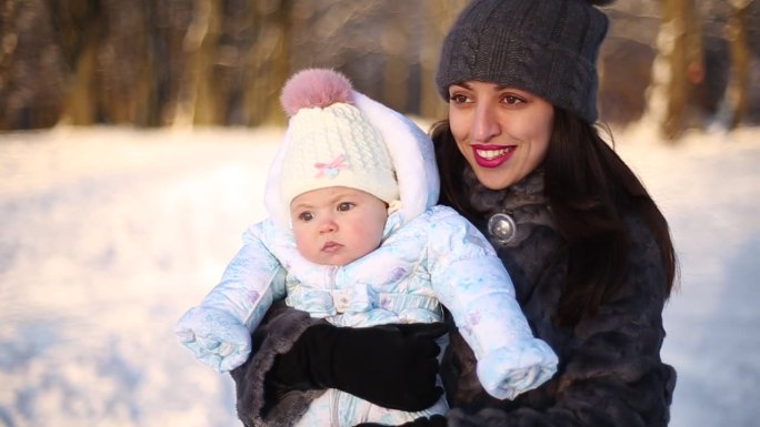 冬日公园里微笑的年轻母亲和孩子的肖像。怀抱小女儿的妇女。