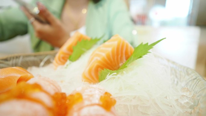 亚洲妇女用筷子夹生鲑鱼，寿司很好吃。