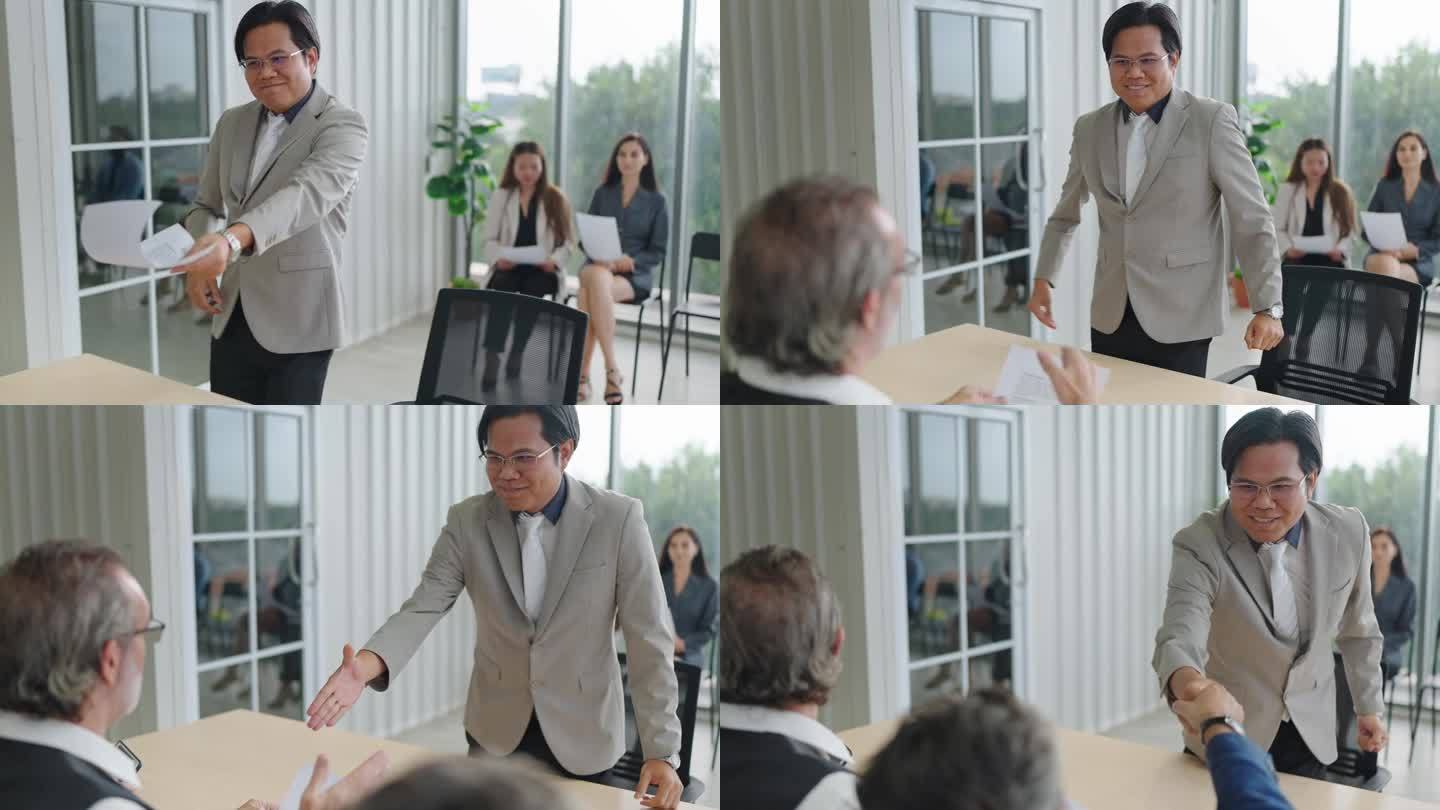 在会议室里，一名亚裔求职者在递简历时与招聘人员握手。求职面试与就业观念