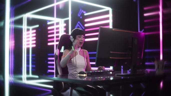 在社交媒体上直播视频游戏。亚洲女孩在未来霓虹灯背景的房间里使用台式电脑。玩家胜利与庆祝