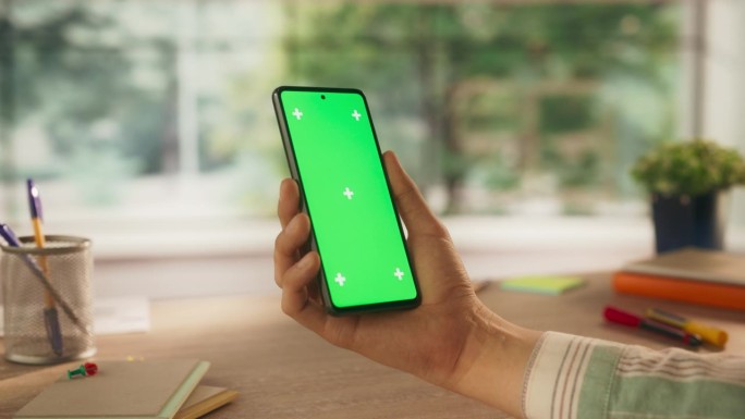 一个普通的人拿着智能手机，看着绿色的Chromakey模拟显示屏。视频模板与数字营销，创意应用程序演