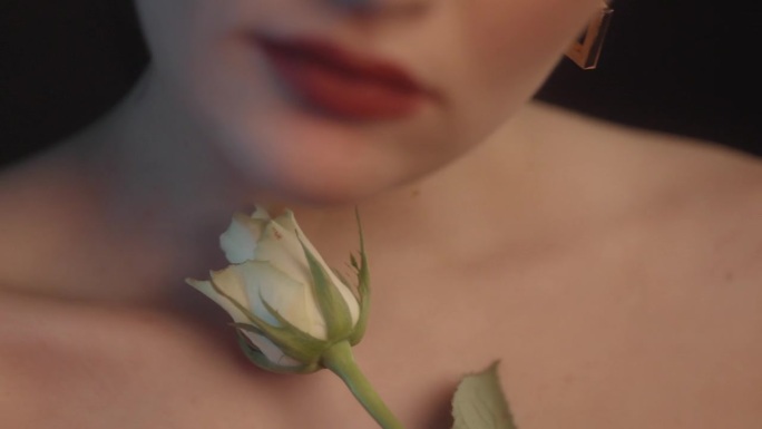 美丽的感性的女人与红色的口红黑色的背景工作室拍摄的姿势与单一的白玫瑰花