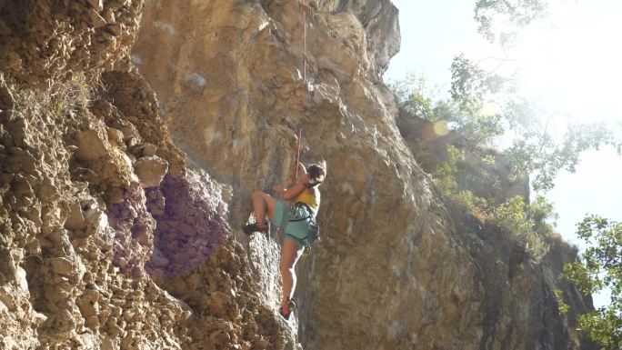 低角度视角:女子顶绳攀爬石灰岩岩壁上具有挑战性的悬挑