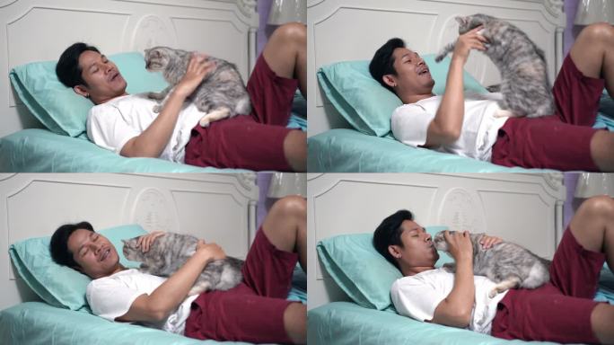 一个亚洲男人躺在卧室的床上和一只猫玩耍