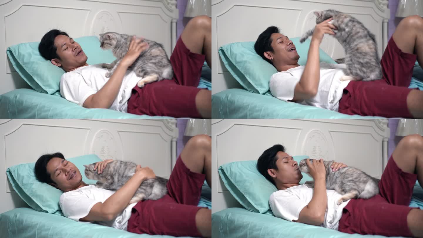 一个亚洲男人躺在卧室的床上和一只猫玩耍