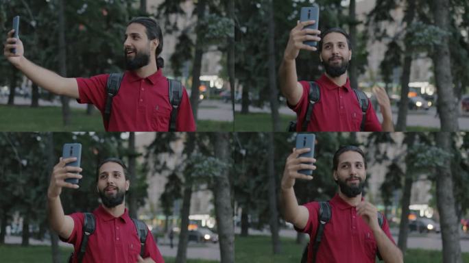有魅力的阿拉伯男子背着背包，用智能手机进行在线视频通话，谈论城市