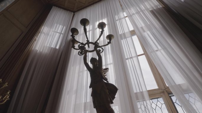 古色古香的石头底座，一个女人举着烛台在她的头上。行动。烛台和窗帘窗户的底部视图