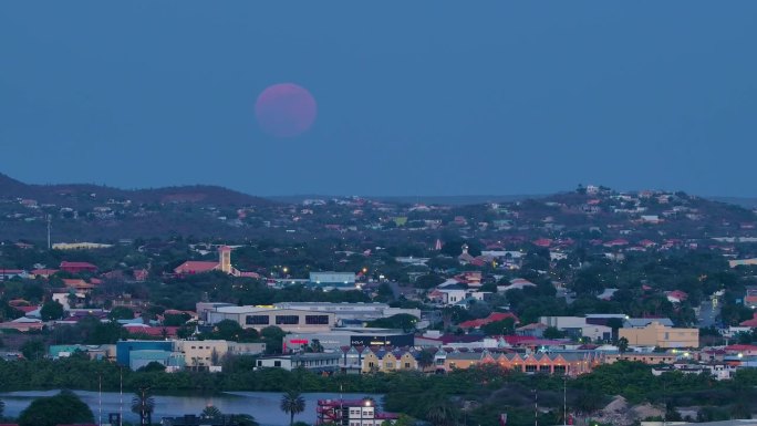 慢慢放大，红紫色的超级月亮在库拉索岛的威廉斯塔德上空缓缓升起