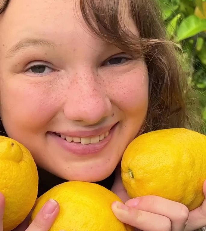 一个十几岁的女孩，穿着白衬衫，金发碧眼，站在一棵柠檬树的背景下，她手里拿着三个摘下来的柠檬，她很开心