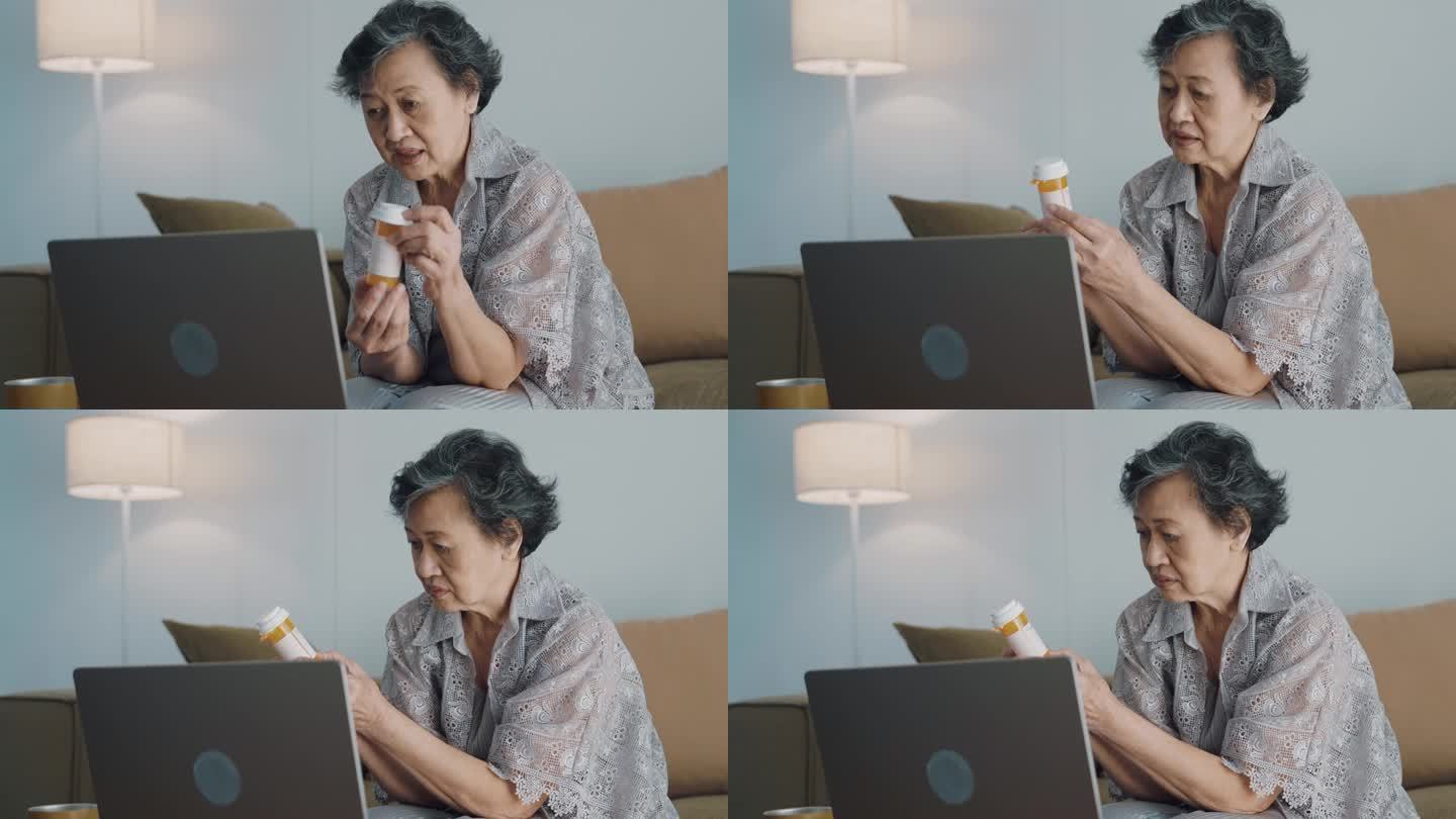 亚洲老年妇女在客厅用电脑，拿着药瓶向医生询问有关药物的问题。