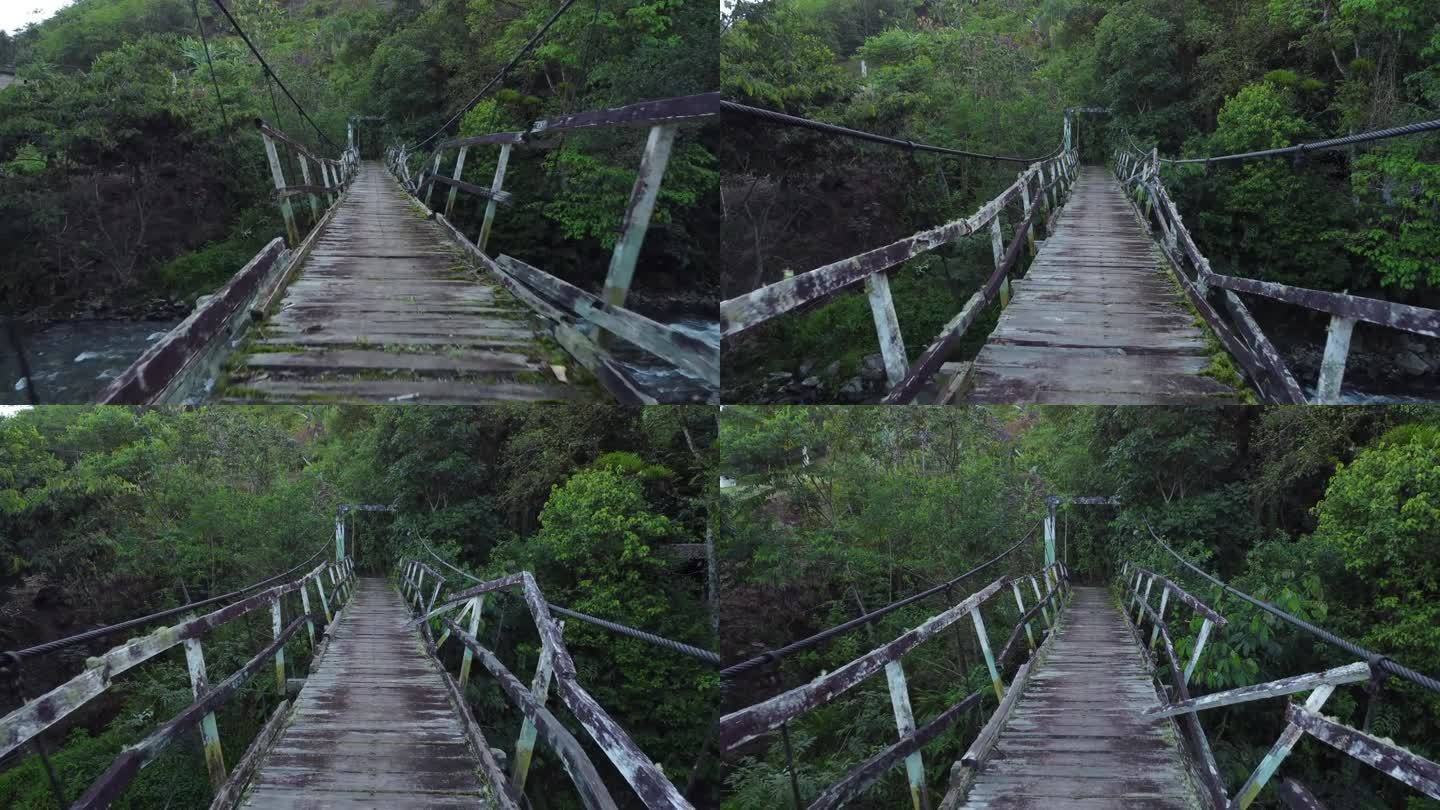 FPV在热带丛林中走过一座破旧的小木桥，桥上有粗金属电缆，下面有一条小河