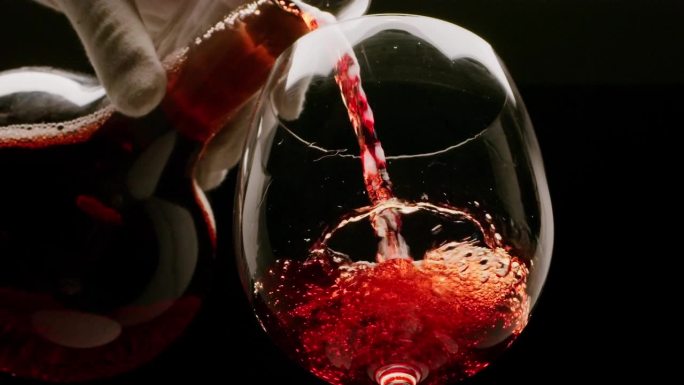 在黑色背景上，红酒正在倒进玻璃杯里。慢镜头，近景。伟大的葡萄酒背景为您的项目。
