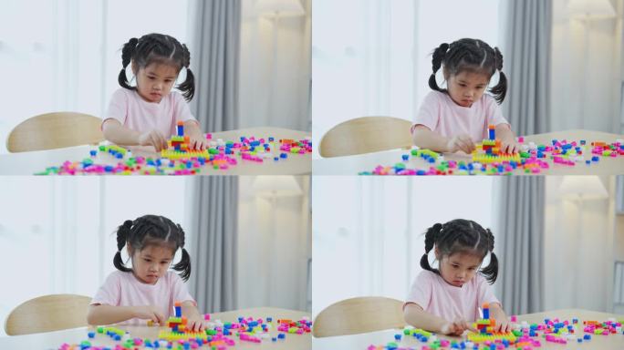 快乐的亚洲女孩开心地笑着玩着五颜六色的乐高玩具，坐在客厅的桌子上，创造性地玩着乐高，搭建着五颜六色的
