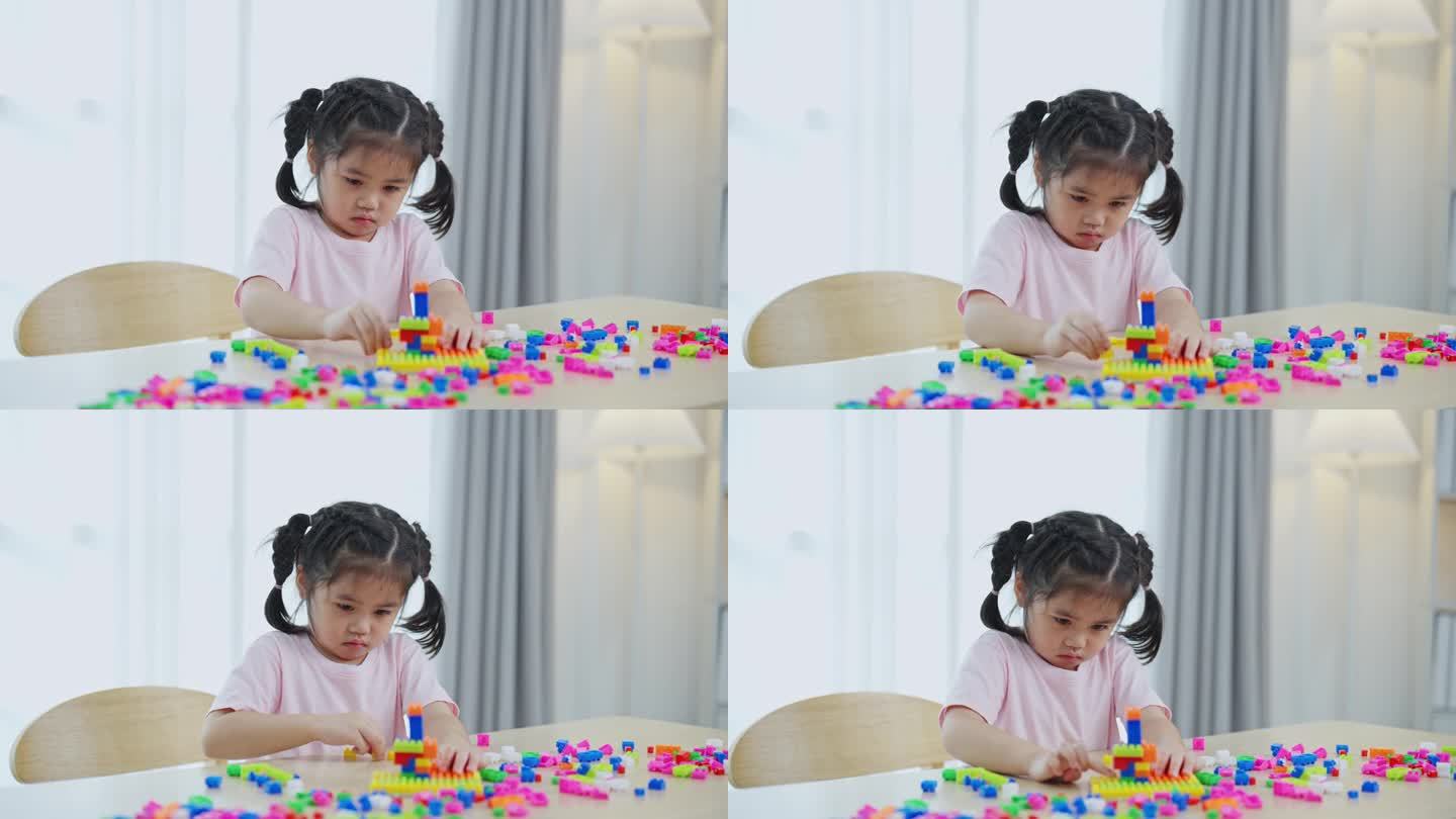 快乐的亚洲女孩开心地笑着玩着五颜六色的乐高玩具，坐在客厅的桌子上，创造性地玩着乐高，搭建着五颜六色的