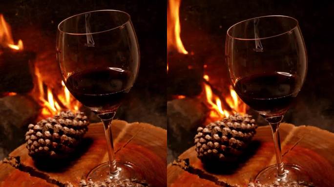 POV:在壁炉旁观察一杯酒的人。木桌上的一杯红酒。壁炉旁的一杯酒。在壁炉里燃烧的木头。喝葡萄酒。在壁