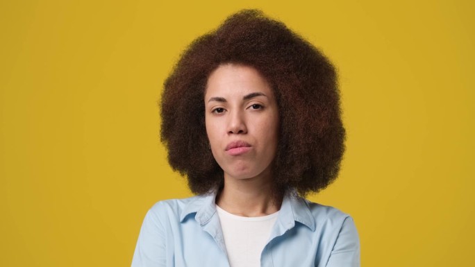 一头卷发的严肃的年轻非裔美国女性站在橘黄色的摄影棚背景下看着摄像机