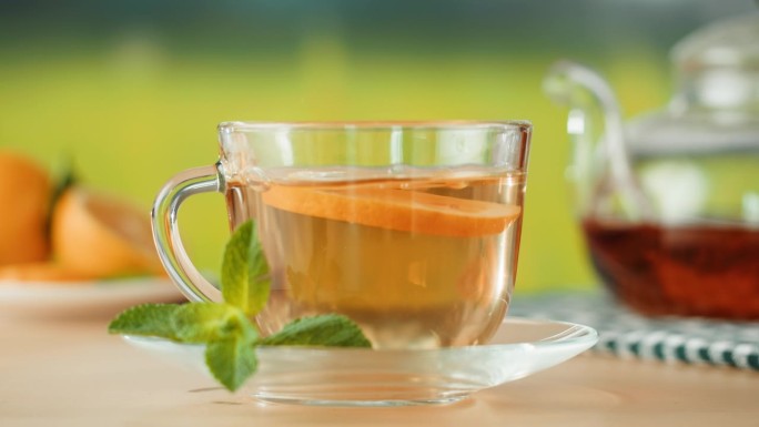 杯中的柑橘茶特写。将橙子放入薄荷茶中，健康的早晨，排毒的热草药饮料。