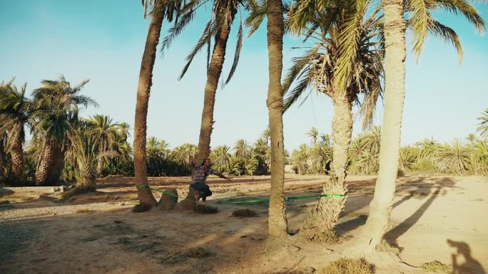 在海滩上，一名年轻人在棕榈树环绕的钢索上走钢丝