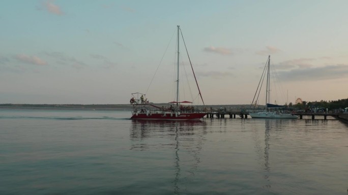 克里米亚刻赤，2021年8月21日刻赤海峡刻赤堤岸。夏天的傍晚，一艘红色的帆船载着人停泊在码头上。骑