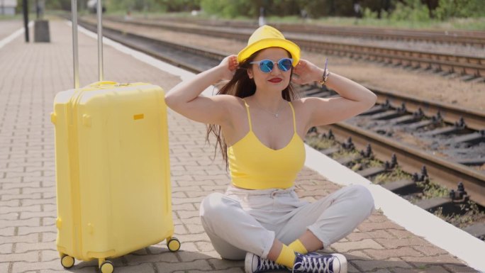 女人的魅力和旅行箱是坐在火车站台上的名片年轻旅行者，等待旅途上的新印象和新会议。女人有一种情绪是快乐