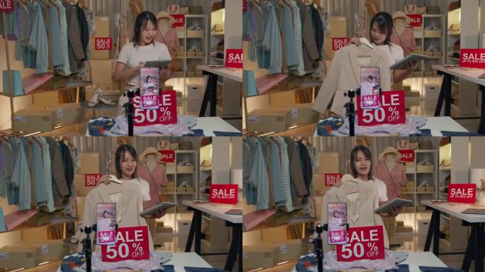 年轻的亚洲女子在晚上通过手机直播向商店里的顾客展示最新的时装系列。中小企业小企业电子商务。