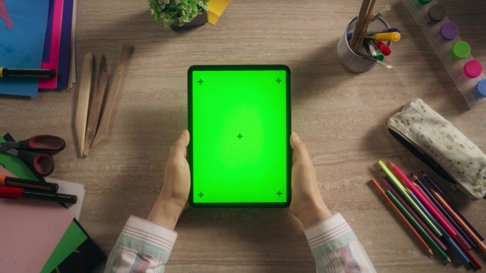 一个匿名的创意年轻人持有平板电脑与模拟绿屏Chromakey显示器垂直俯视视图。设计师或艺术学生观看