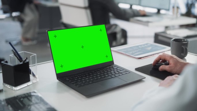 成功的白人商人坐在办公桌旁用绿屏笔记本电脑工作。匿名商人使用色度键显示。时尚明亮的工作场所。过肩特写