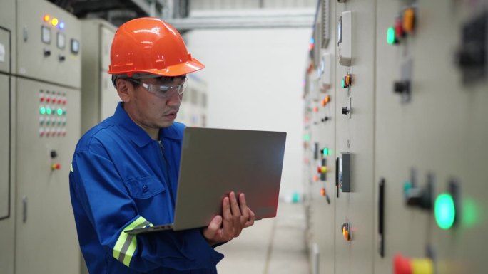 电气工程师勤奋地检查和控制开关机房的电气系统，利用先进的技术和笔记本电脑，以确保工厂电力的顺利运行。